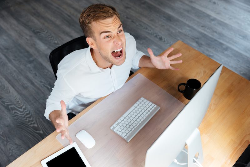 A business man is mad and sits at his desk.